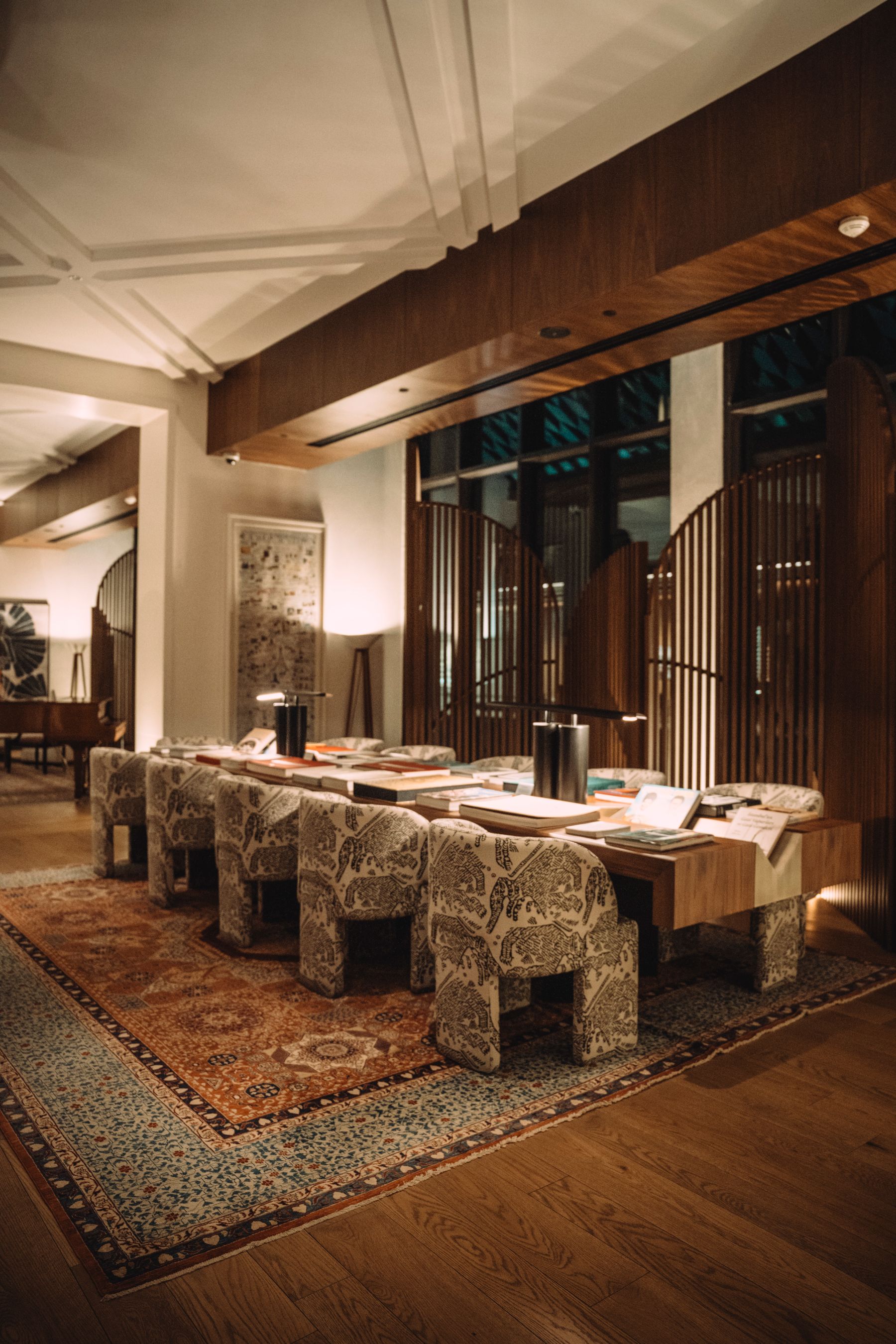 A warmly lit hotel lounge with timber screens and a long reading table at night — illustrative photography